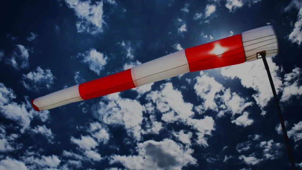 Red and white wind direction flag under a blue sky with clouds